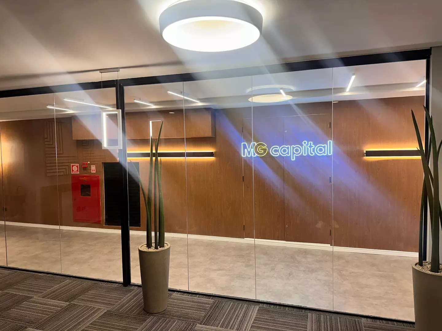 Recepção da MG Capital com o nome da empresa em neon na parede de madeira